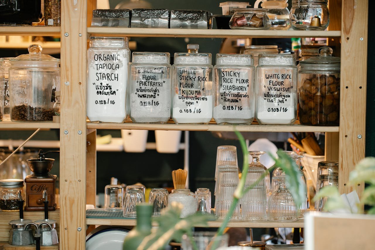 A variety of flour jars displayed on a wooden pantry shelf with plants.